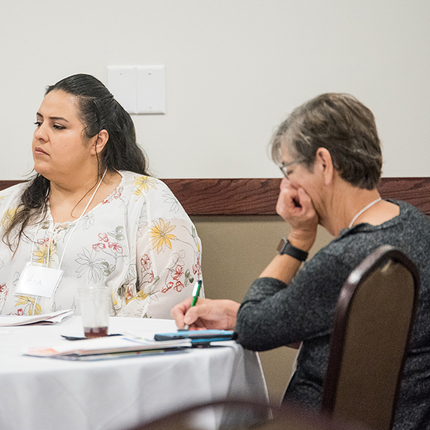 women sitting at a table, listening and taking notes