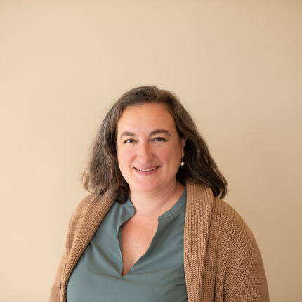 White female posing for headshot in front of tan wall