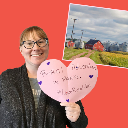 Mujer sosteniendo un corazón que dice "Aventuras rurales en parques #LoveRuralAm"