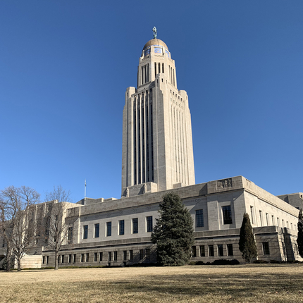 Edificio del Capitolio del Estado de Nebraska: un edificio plano de granito de dos pisos con una aguja que se eleva en el medio y una cúpula de bronce en la parte superior.