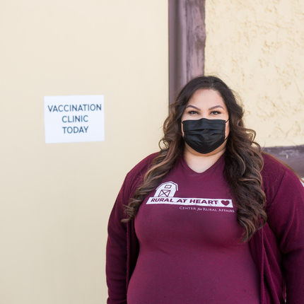 Mujer de pie frente a una puerta con un cartel que dice "Clínica de vacunación hoy".