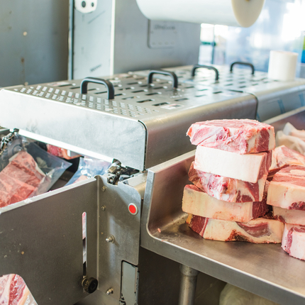 Foto del procesamiento de carne: carne envasada saliendo de la máquina de envasado en plástico y carne cruda apilada en el mostrador.