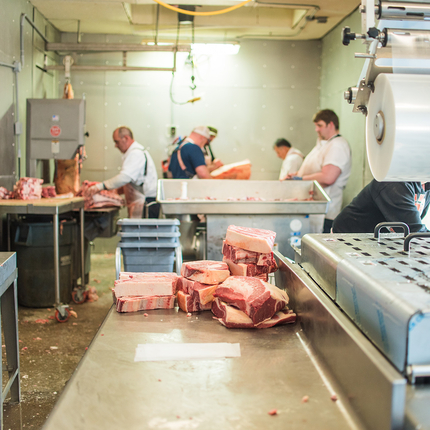 Red meat sitting on a counter with people processing meat in the background