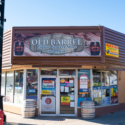 Store front with large sign on top and doors and windows with signs and two barrels on each side of the doors