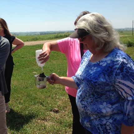 woman holding measuring cup, while other woman tests the soil
