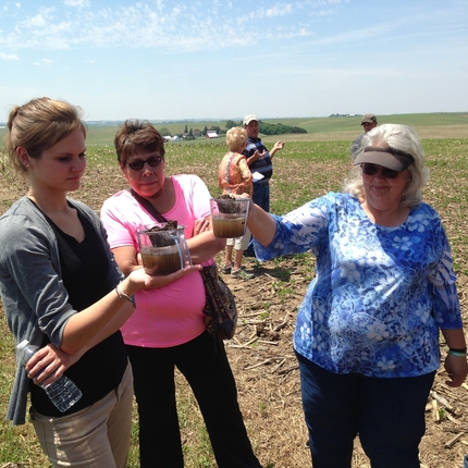 2 women holding measuring with water and soil in them, 1 woman looks on
