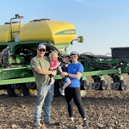 A man and woman in ball caps holding two small children standing in front of a planter