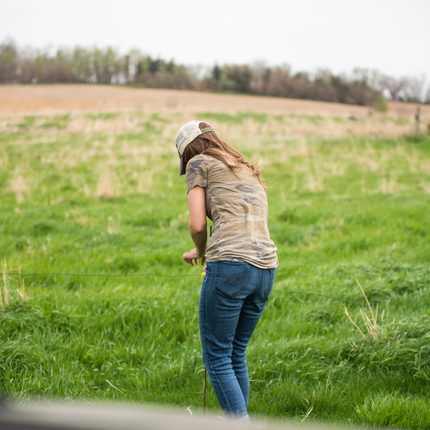 Woman wearing hat, T-shirt and jeans examining grazing grasses