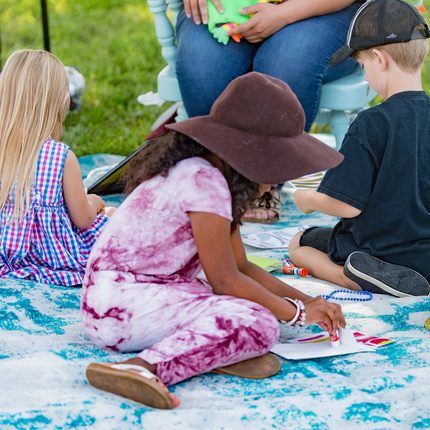 Children doing art projects while sitting on a blanket in a grassy area