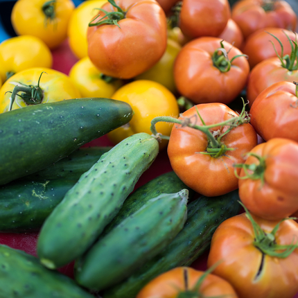 Una pila de verduras sobre una mesa, incluidos pepinos verdes y tomates amarillos y rojos.