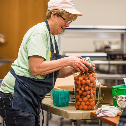 Woman cafeteria worker adding cherry tomatoes to a clear container for lunch service