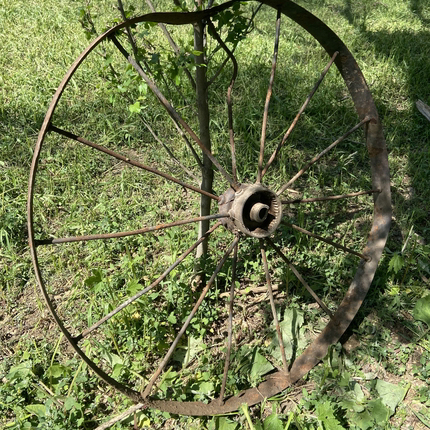 A metal wagon wheel that's a little bent, leaning against a fence post