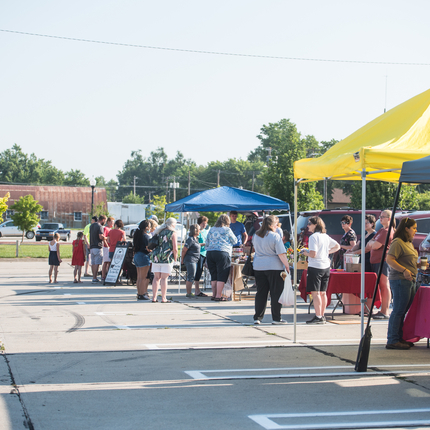 A row of farmers markets booths with blue and yellow tents.