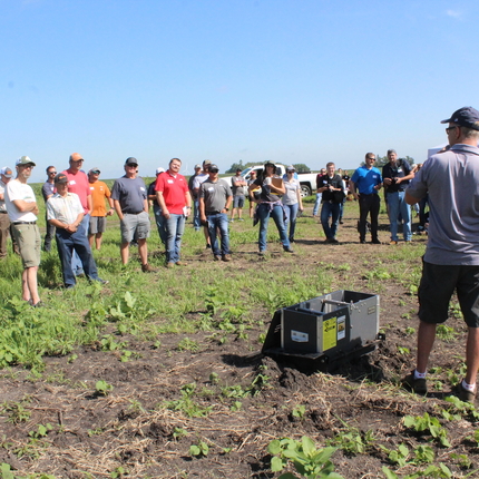 Group of people in a farm field listening to a speaker 