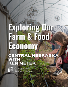 Two people kneel inside a greenhouse, closely examining young green plants growing in rows with drip irrigation lines. Large fans hang overhead, and soft natural light fills the space. Text on the image reads, “Exploring Our Farm & Food Economy – Central Nebraska with Ken Meter,” alongside the Center for Rural Affairs logo.