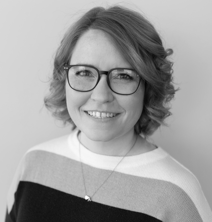 Fotografía en blanco y negro de una mujer sonriendo a la cámara, con cabello claro hasta los hombros y gafas de montura oscura.