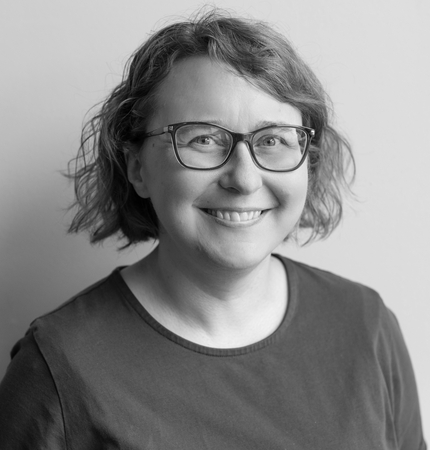Woman smiling at the camera with short curly hair, glasses, and a dark colored shirt