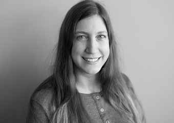 black and white photo of a woman smiling at camera, with dark, long hair and a button-up shirt