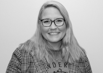 black and white photo of a woman smiling at the camera, with light shoulder-length hair and dark-rimmed glasses