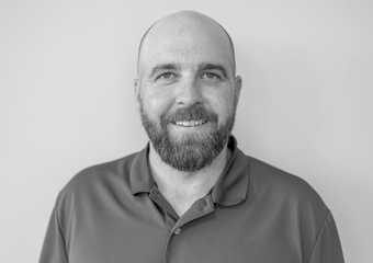 Bald man with a beard and mustache, wearing a dark colored polo shirt