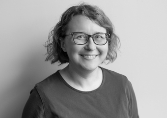Woman smiling at the camera with short curly hair, glasses, and a dark colored shirt