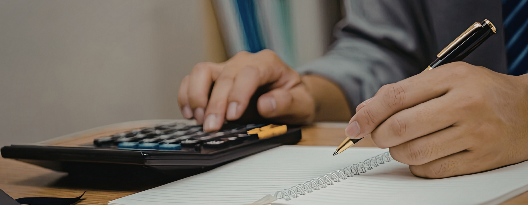 Hands type on a calculator and write in a notepad