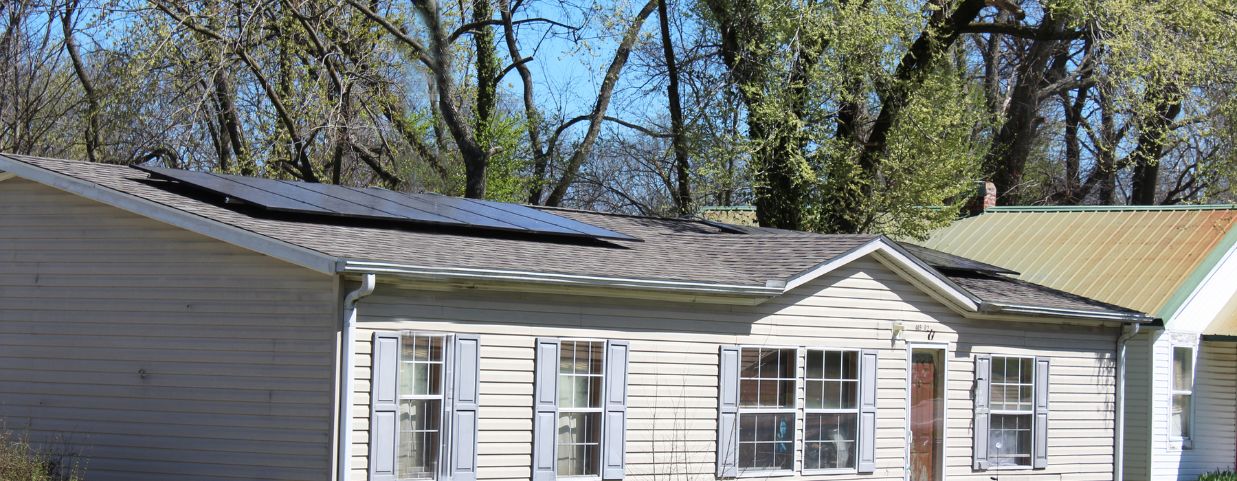 Casa de un piso, color blanquecino, con dos paneles solares separados en el techo.