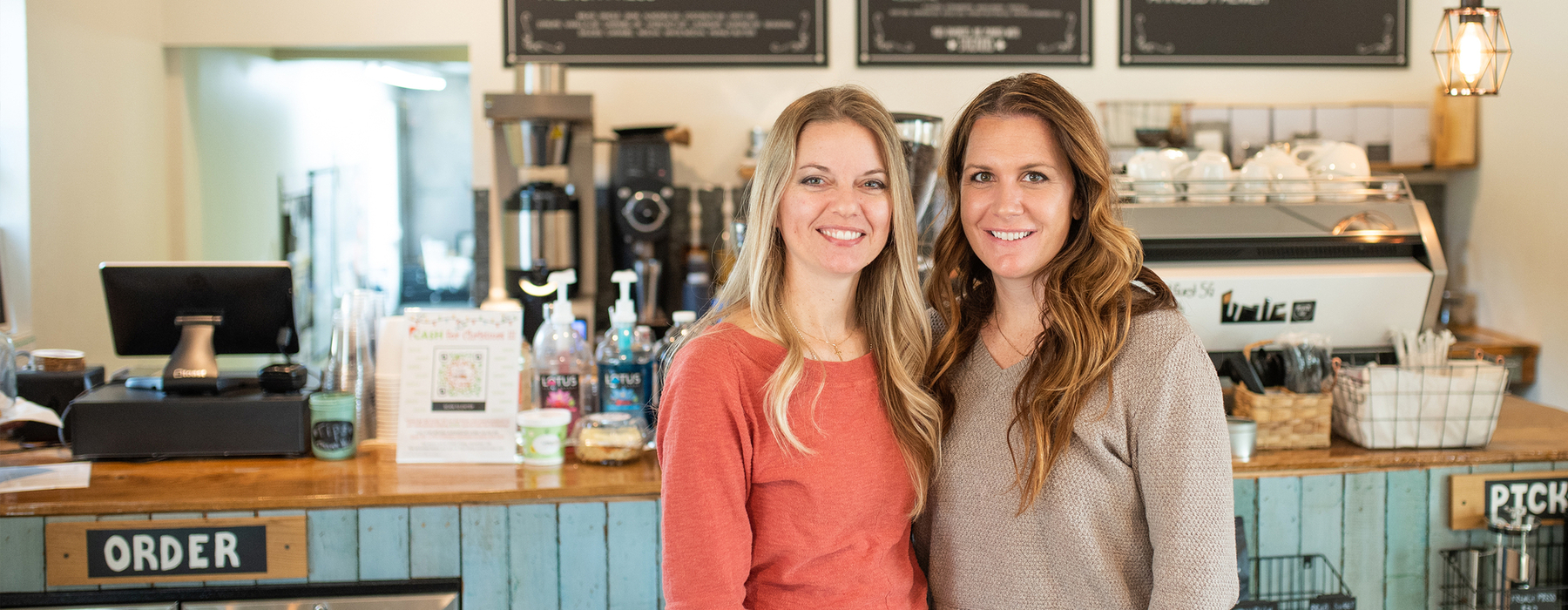 Two women stand at coffee shop counter