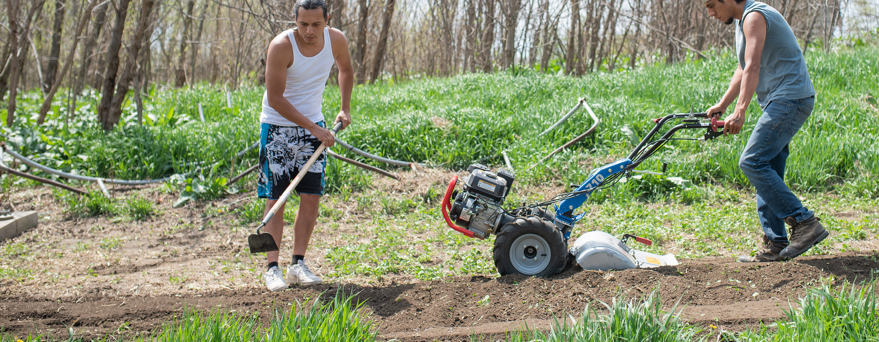 Two Native American men tilling a garden with a manual till and motorized tilling machine.
