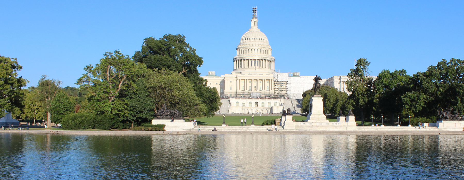 US Capitol building view from the west, with a reflecting pool in the foreground, with a blue sky behind the building