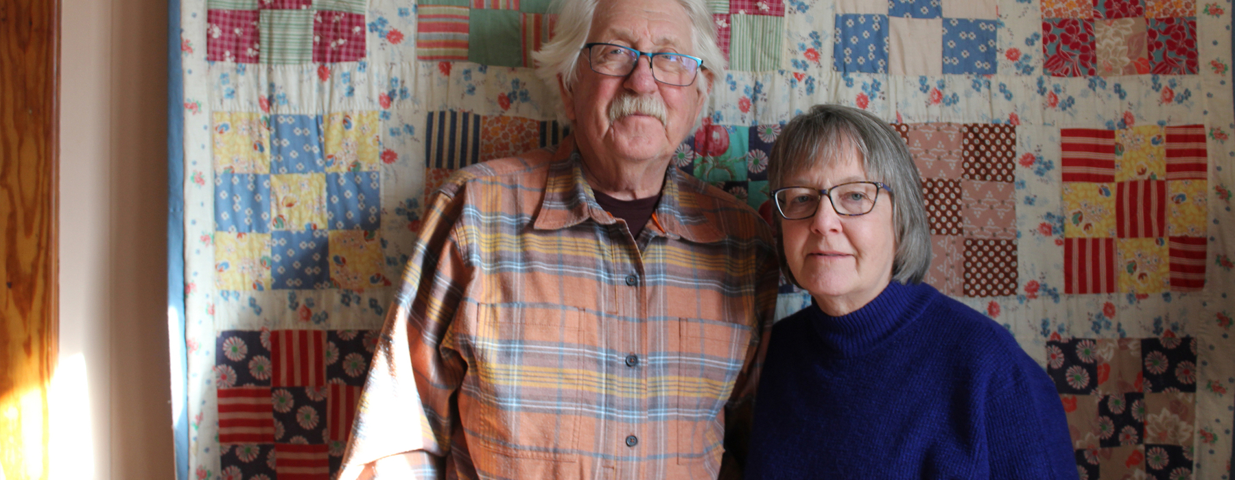 Man and woman stand in front of a quilt hanging on the wall